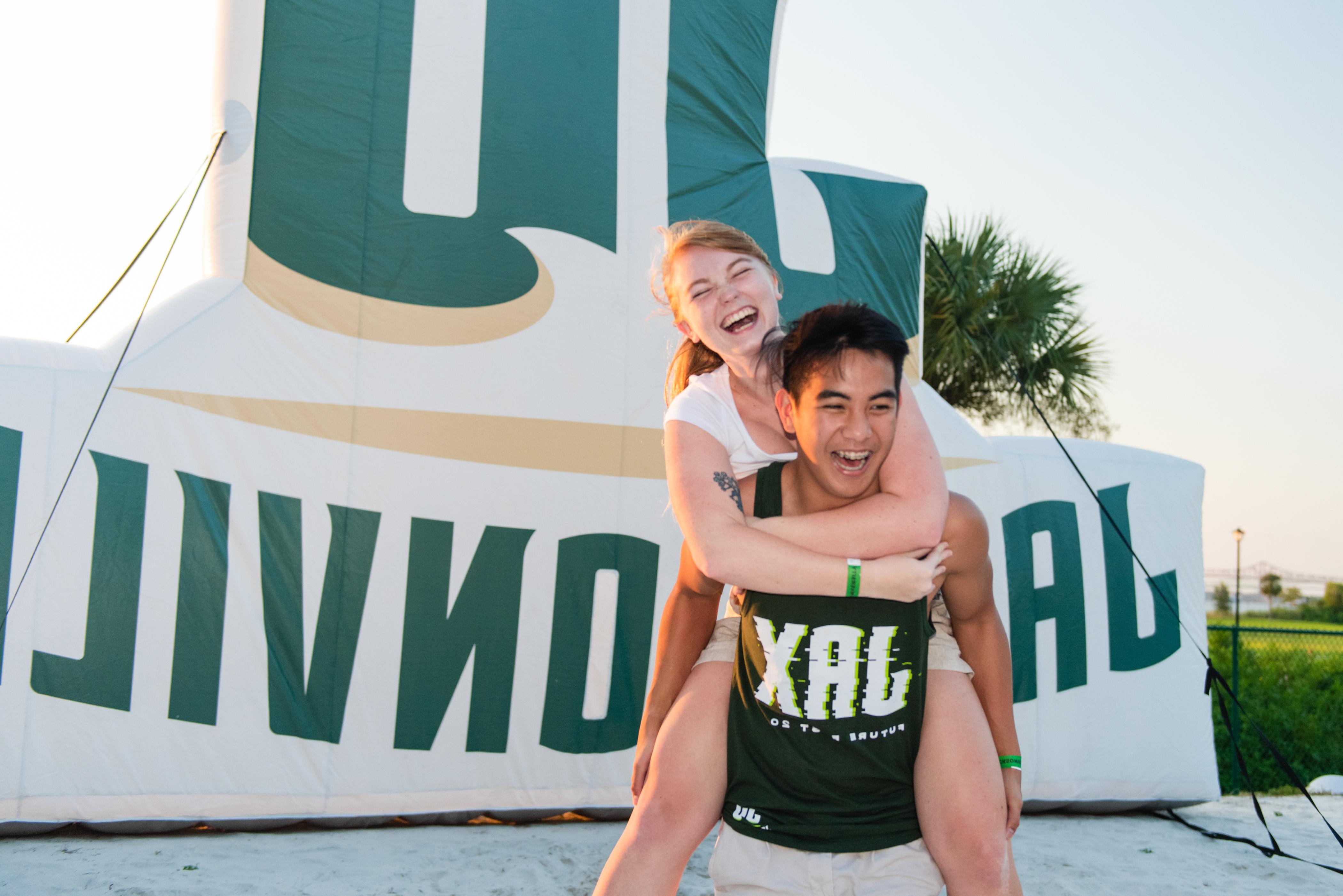 Two students piggy-backing in front of a JU inflatable. 